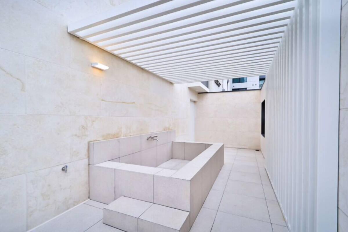 A modern bathroom with a large bathtub, tiled walls, and a slatted ceiling.