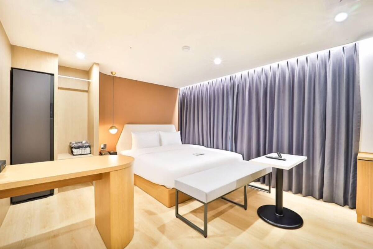 A modern hotel room with a bed, bedside table, and a desk with a chair.