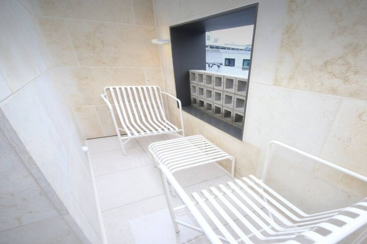 A modern outdoor seating area with white metal chairs and a small table, adjacent to a building with a tiled facade.