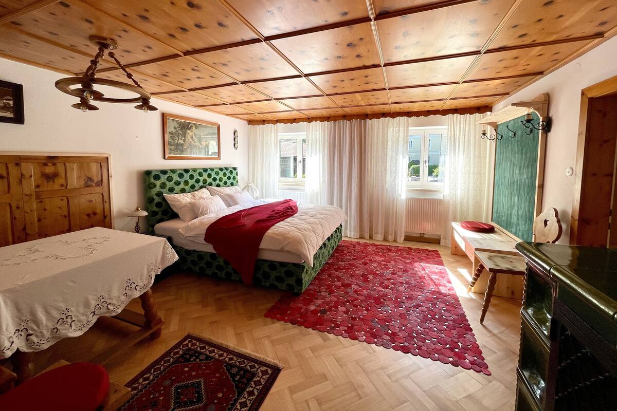 A room with a wooden ceiling, a bed with a green headboard, a red rug, and a wooden dresser.