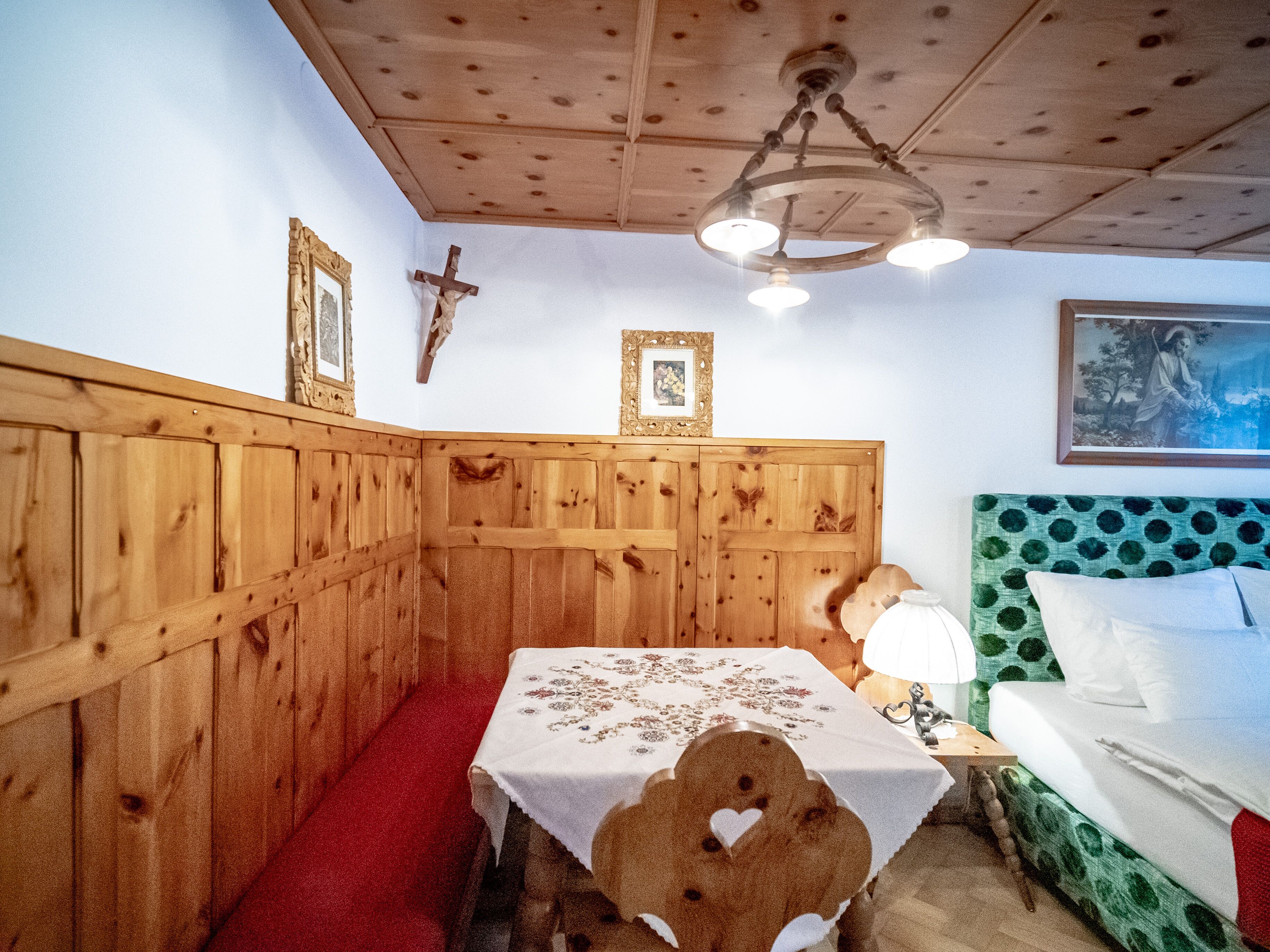 A wooden room with a table, a cross, and a painting on the wall.