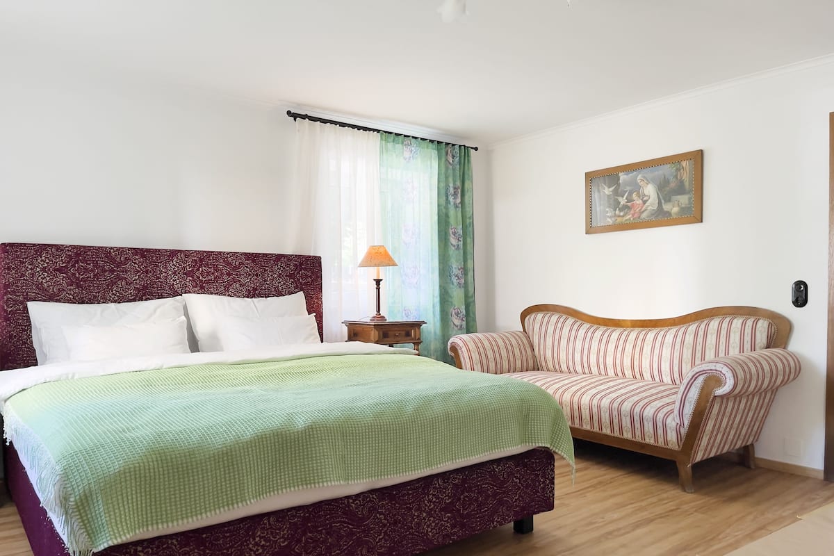 A bedroom with a large bed, a wooden nightstand, a striped armchair, and a painting on the wall.