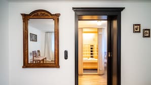 A hallway with a wooden floor, a mirror with a wooden frame, and a door leading to a room with a bed and a nightstand. - Katzerhaus Ebensee (Ebensee)