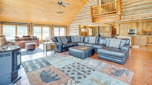 A spacious log cabin interior with a large living area, a fireplace, and a kitchen.