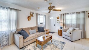 A living room with a beige sofa, a wooden coffee table, a white armchair, and a ceiling fan.