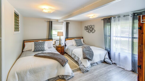A bedroom with two beds, a nightstand, a lamp, and a window with curtains.
