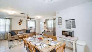 A well-lit living room with a sofa, dining table set for four, and a kitchen area with a microwave.