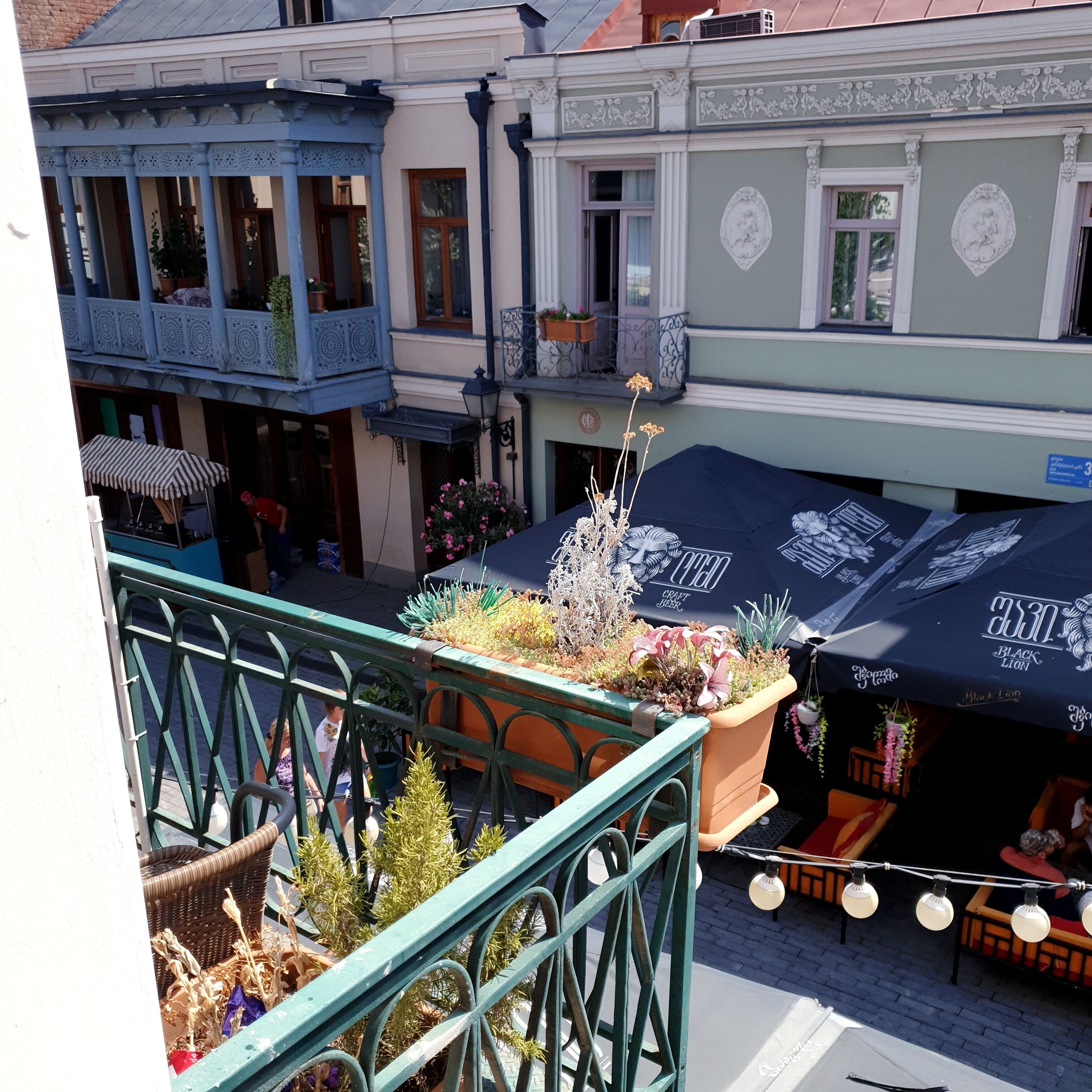 A courtyard with a blue building, a green building with a balcony, and a black umbrella with 'Black Lion' branding.