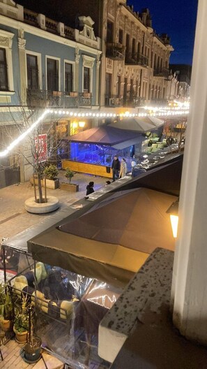 A nighttime view of a street with buildings, a covered outdoor seating area, and a few people. - Historic Apartments "1868 Tbilisi" Best Location (Tbilisi)