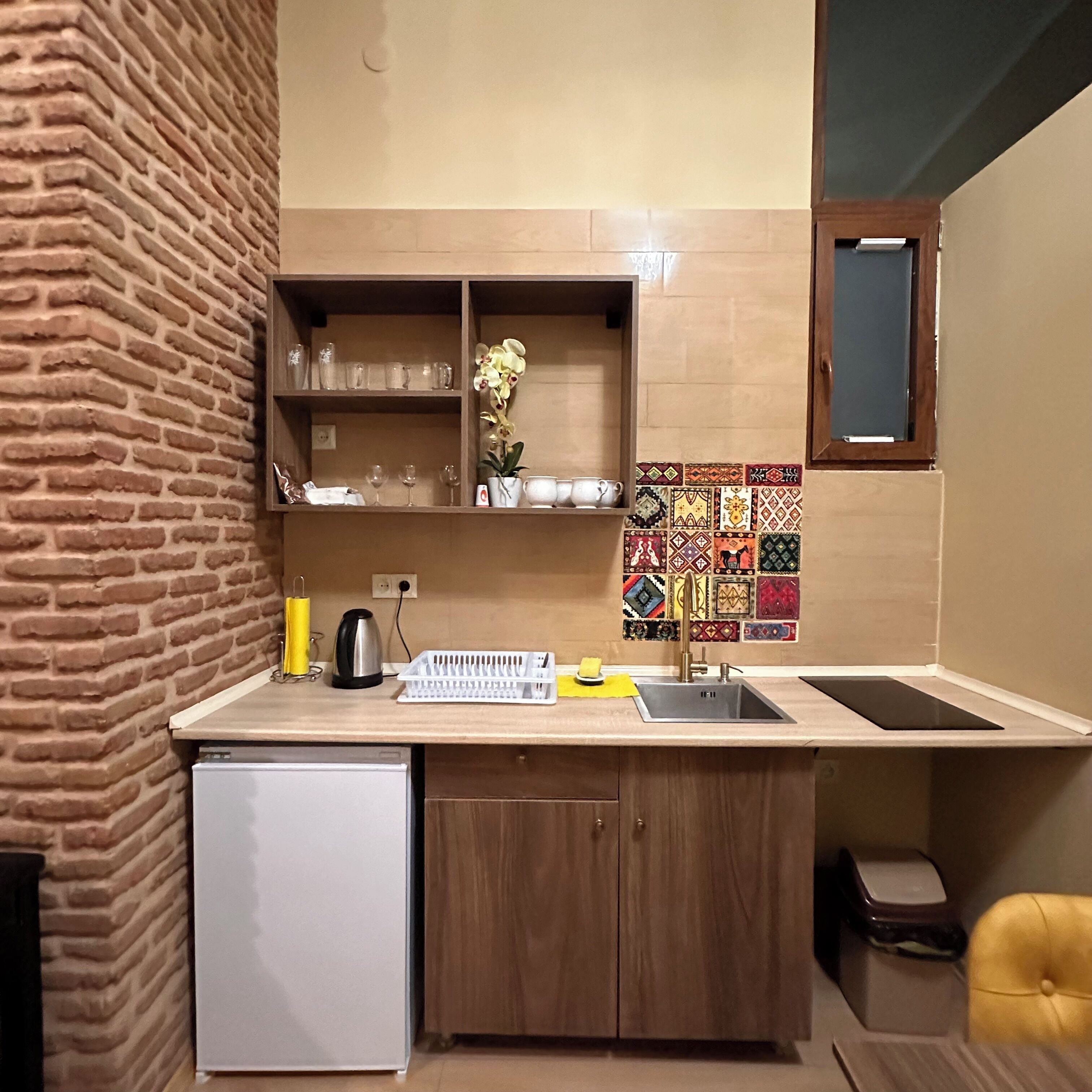 A compact kitchen with a refrigerator, a sink, and a small cabinet. There is a window with a view of the outside.