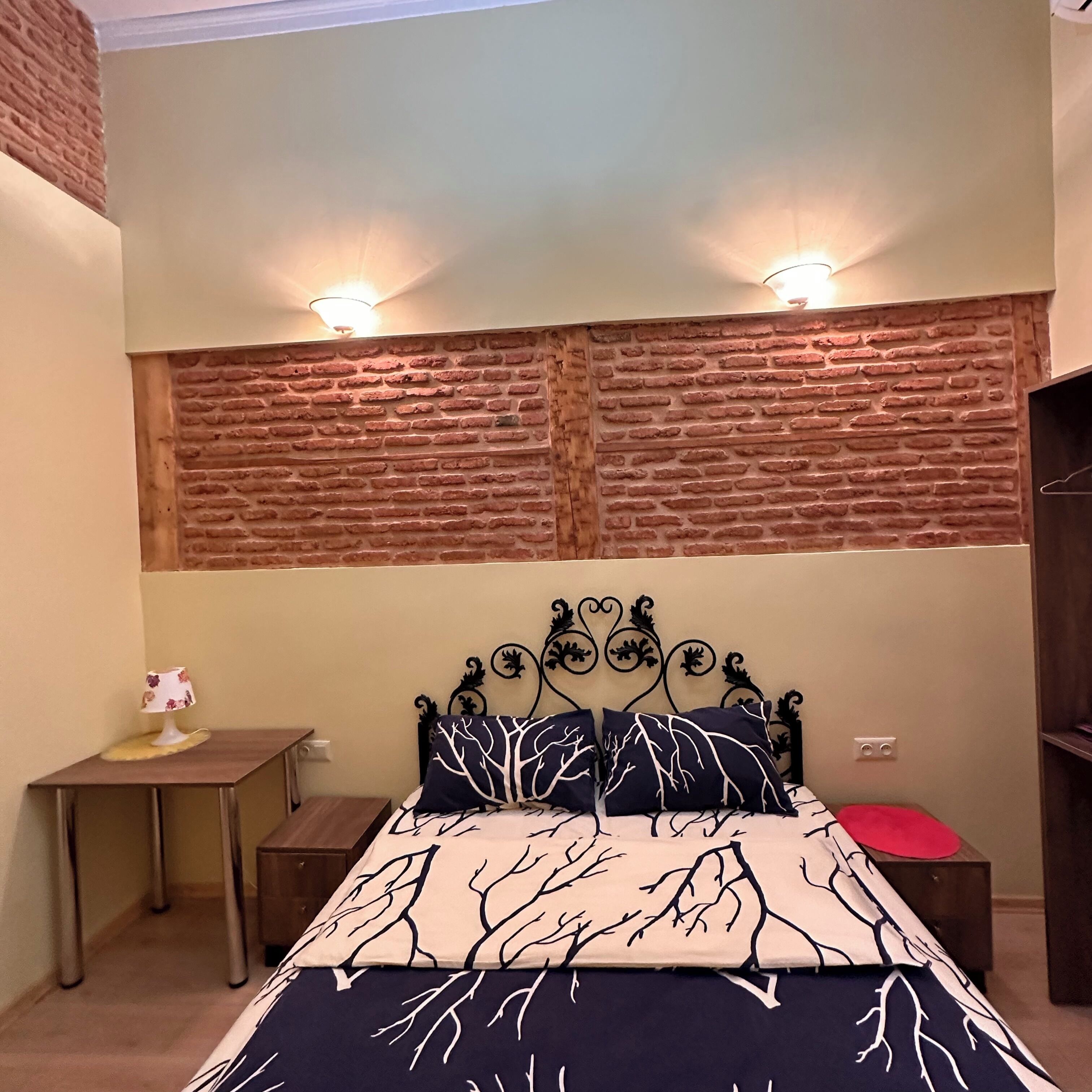 A bedroom with a bed, two bedside tables, a small table with a decorative item, and a brick-patterned wall.