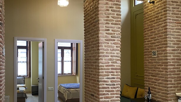 Una habitación amplia con paredes de ladrillo visto, piso de madera y una cama al fondo.