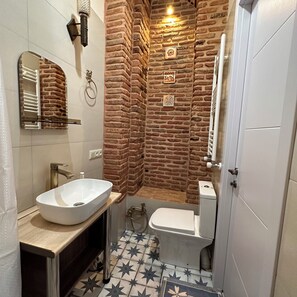 A bathroom with a white sink, a toilet, and a shower area with a brick wall design. - Historic Apartments "1868 Tbilisi" Best Location (Tbilisi)