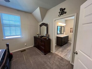 Cozy apartment with a loft-style design, featuring a large dresser, window, and door to a bathroom with a double mirror.