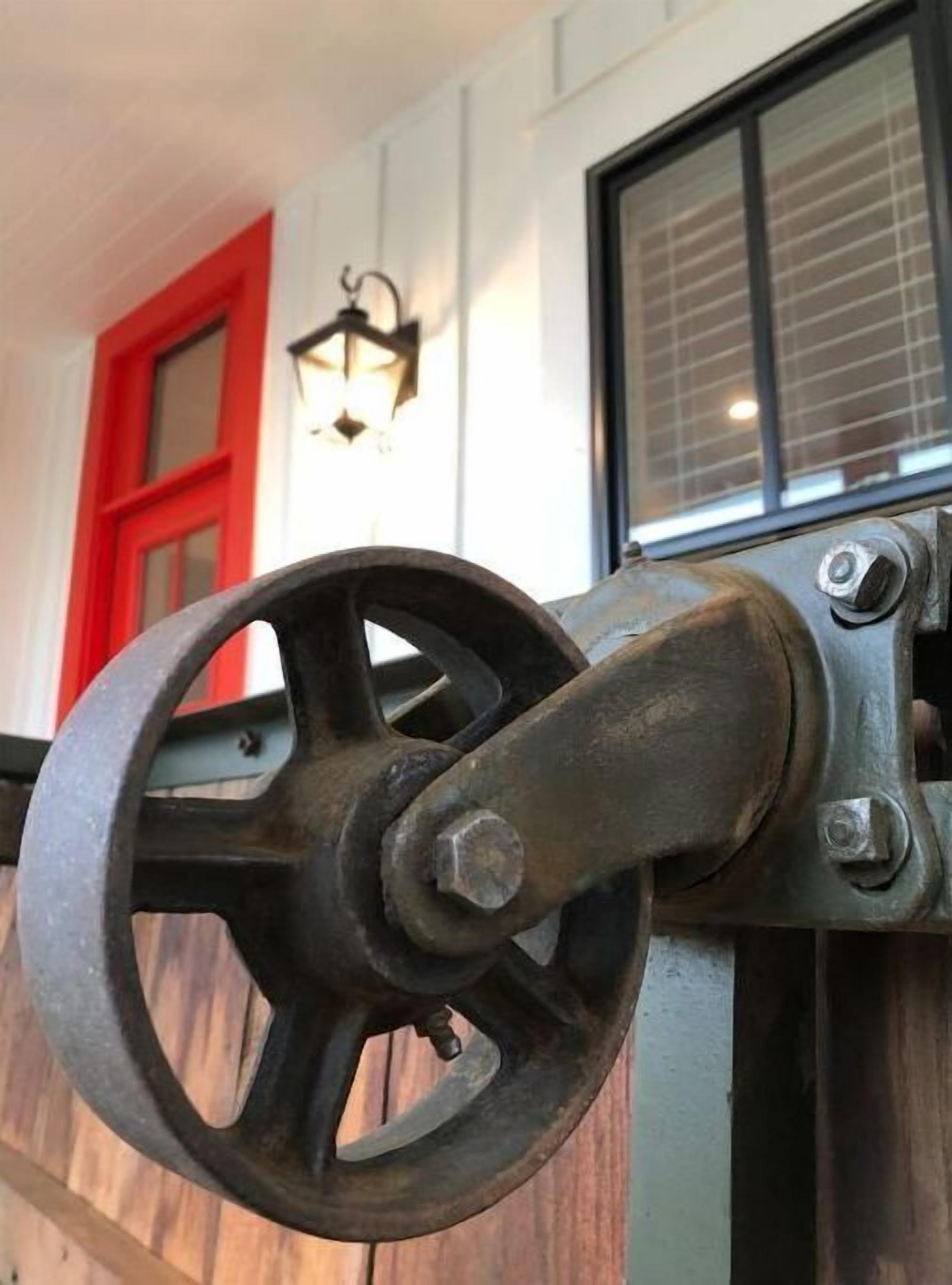 Primer plano de una rueda mecánica, posiblemente parte del mecanismo de una puerta o ventana, con un tornillo y tuerca visibles.