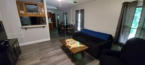 A living room with a sofa, a coffee table, a TV stand, and a dining area with a table and chairs.