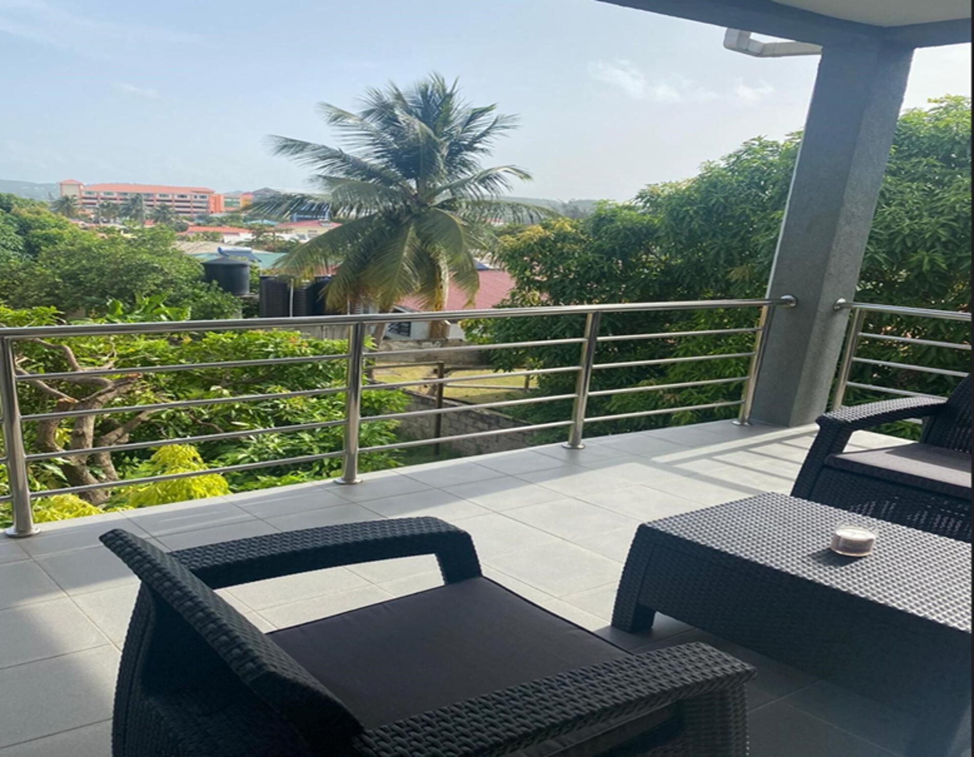 A balcony with wicker furniture, a metal railing, and a view of greenery and buildings in the distance.