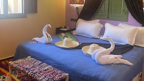 Habitación de hotel con una cama, un banco tejido colorido, un adorno de pared y una ventana con cortinas.