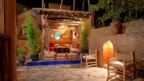 Un patio exterior con suelo de piedra, mobiliario de madera y plantas en macetas.