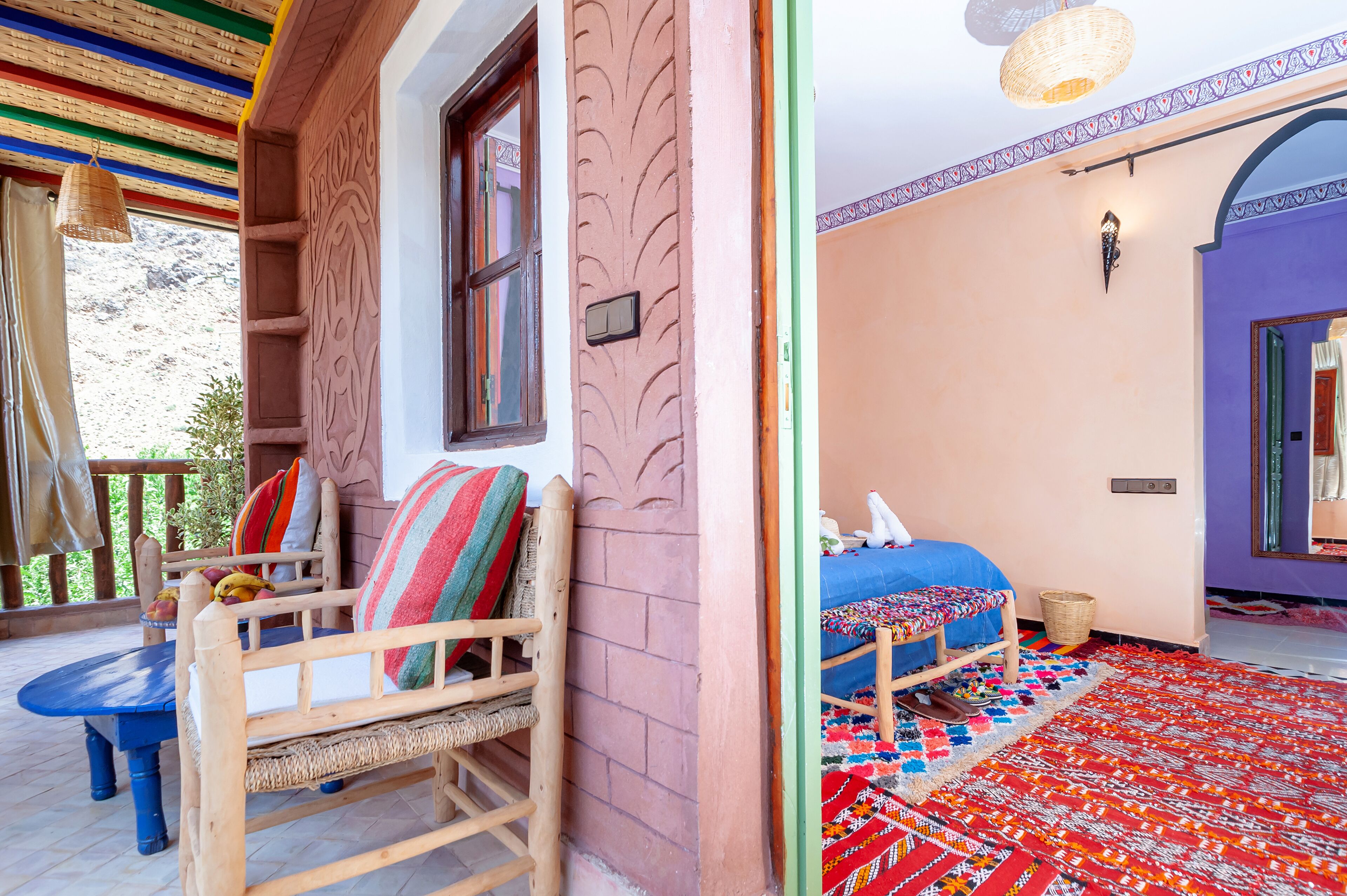 Una habitació amb un llit, una cadira, una taula petita i una catifes colorida.