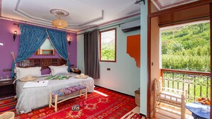 Una habitación con cama, un banco, una ventana con vistas a la vegetación y un balcón con mesa y sillas.