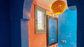 Un baño con piso a cuadros, un inodoro, un lavamanos con espejo decorativo y una lámpara colgante.