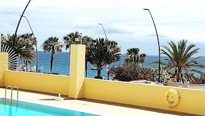 Ein Poolbereich mit Blick auf den Ozean, Palmen und einem Rettungsring an der Wand.