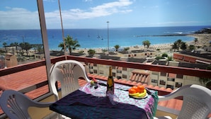 Ein Balkon mit Tisch für zwei Personen, mit Blick auf einen Strand mit Booten und Gebäuden.