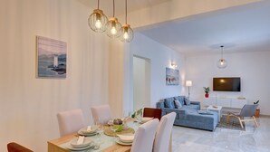 Un salon moderne avec un canapé, un téléviseur et un coin repas avec une table dressée pour quatre personnes.