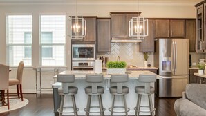 Una cocina moderna con una isla central, taburetes de bar, electrodomésticos de acero inoxidable e iluminación colgante.