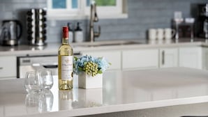 Una encimera de cocina con una botella de vino, dos copas y un ramo de flores.