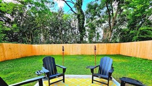 Ein Garten mit einer gelb gemusterten Terrasse, zwei Adirondack-Stühlen und einem Holzzaun.