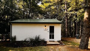 Eine kleine, eingeschossige Holzhütte mit einem grünen Dach, umgeben von dichtem Baumbestand.