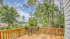 A wooden deck with a table and chairs, surrounded by trees and a view of a body of water.