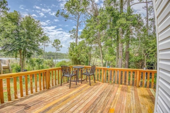A wooden deck with a table and chairs, surrounded by trees and a view of a body of water.
