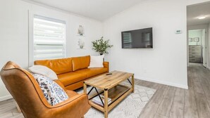 A modern living room with a brown leather sofa, a wooden coffee table, and a white wall with a mounted television.