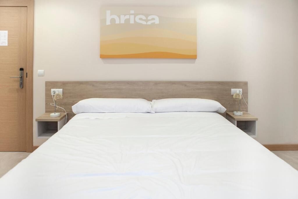 Ein Hotelzimmer mit einem großen Bett, zwei Nachttischen mit Lampen, einem hölzernen Kopfteil und einem an der Wand hängenden Kunstwerk mit dem Schriftzug 'brisa'.