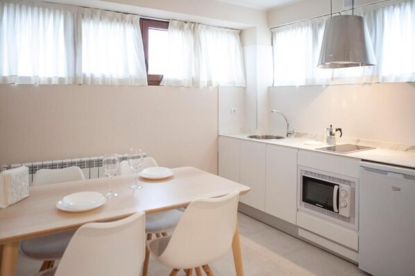 A compact kitchen with a built-in oven, a sink, and a dining area with a table and chairs. - Apartamentos La Canal (Santa Cruz de Bezana)