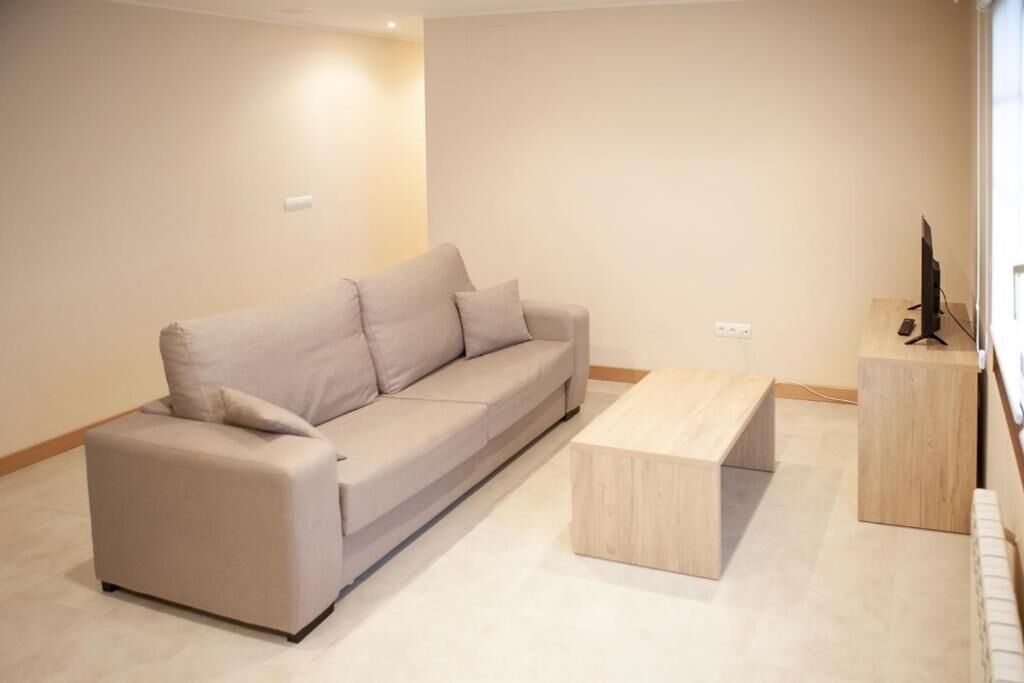 A modern living room with a beige sofa, a wooden coffee table, and a television on a wooden stand.