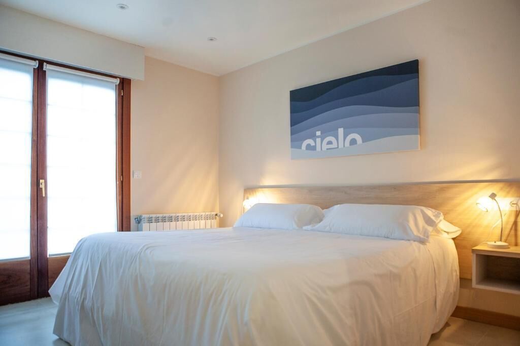 Une chambre à coucher comprenant un lit, une table de chevet, une lampe fixée au mur et une fenêtre avec des stores.
