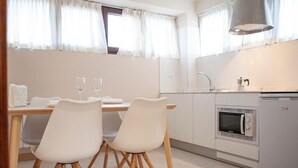 A modern kitchen with white cabinetry, a built-in oven, and a dining area with two white chairs and a table.