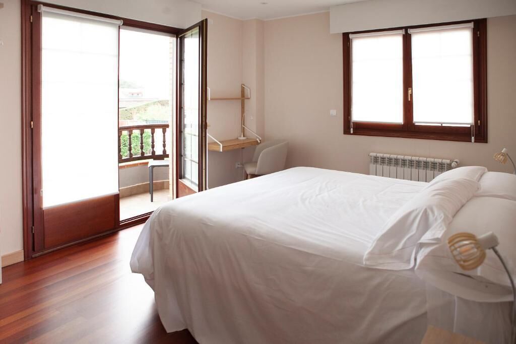 A bedroom with a bed, a desk, and a chair. There is a sliding door leading to an outdoor area.