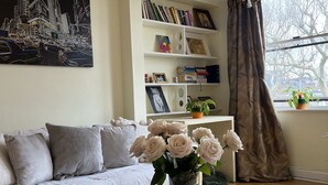 Un salon avec un canapé, une table basse sur laquelle se trouve un livre, une bibliothèque et une fenêtre avec des rideaux.