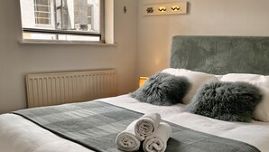 Un lit bien fait, recouvert d’une couvre-lit à motifs gris et blancs, avec deux oreillers gris et une serviette blanche roulée posée sur le lit.