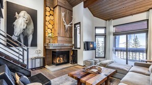 A spacious living room with a fireplace, a large window with a view of the outdoors, and a staircase with a modern design.