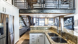 A modern kitchen with granite countertops, stainless steel appliances, and a double-height staircase.