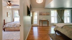 A bedroom with a wooden floor, a bed, a ceiling fan, a table, and a TV mounted on the wall. - Gorgeous country cottage (Springfield)