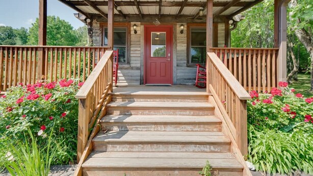 A wooden porch with a red door, wooden railings, and steps leading to a covered area. - Gorgeous country cottage (Springfield)
