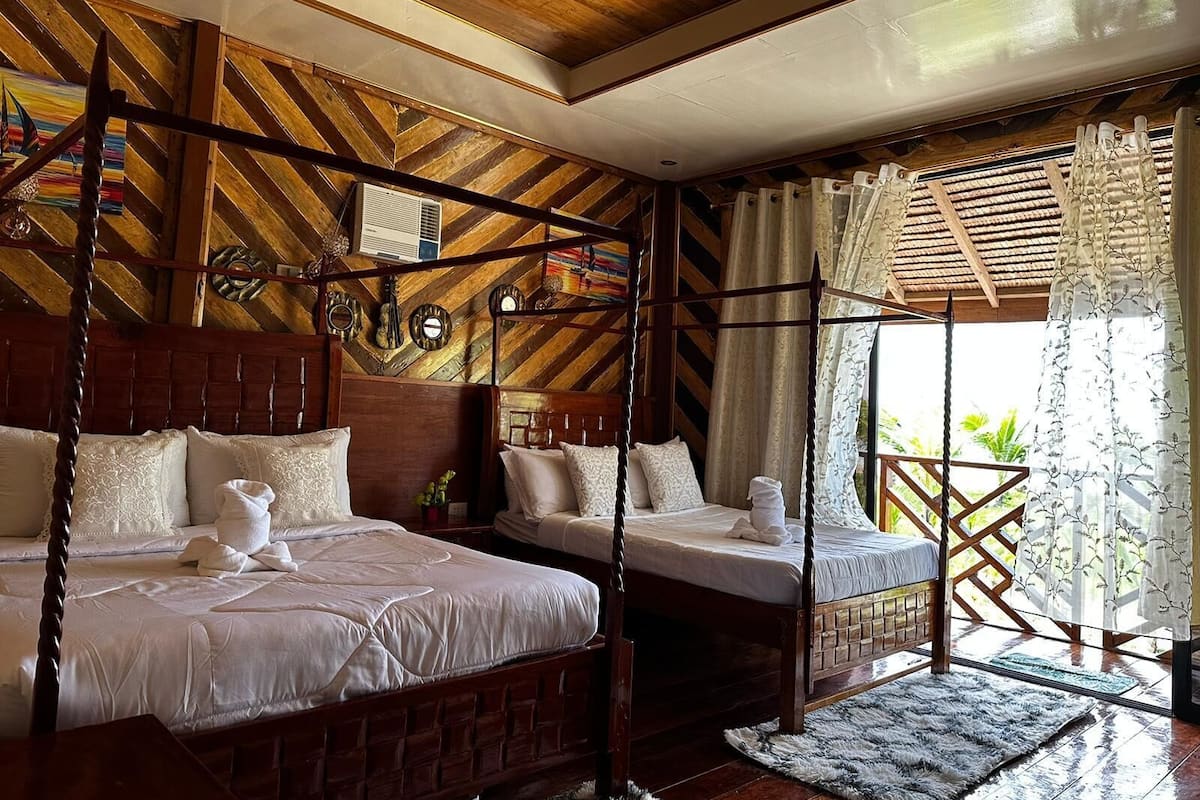 Een kamer met twee houten bedden, een plafondventilator en uitzicht op groen.