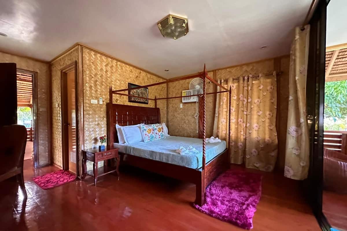 Een bed met hemelbed, met een houten frame en hoofdbord, een klein nachtkastje en een roze vloerkleed.